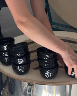 A person is unloading the ceramic kiln, stacking finished cups of a comissioned custom order onto each other
