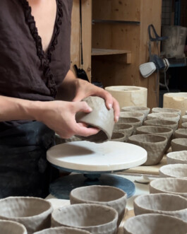 A person forming a cup by hand. Lots of cups of the same comission are placed around the work area.