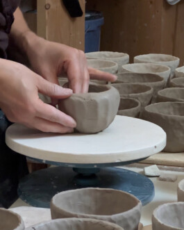 A person forming a cup by hand. Lots of cups of the same comission are placed around the work area.